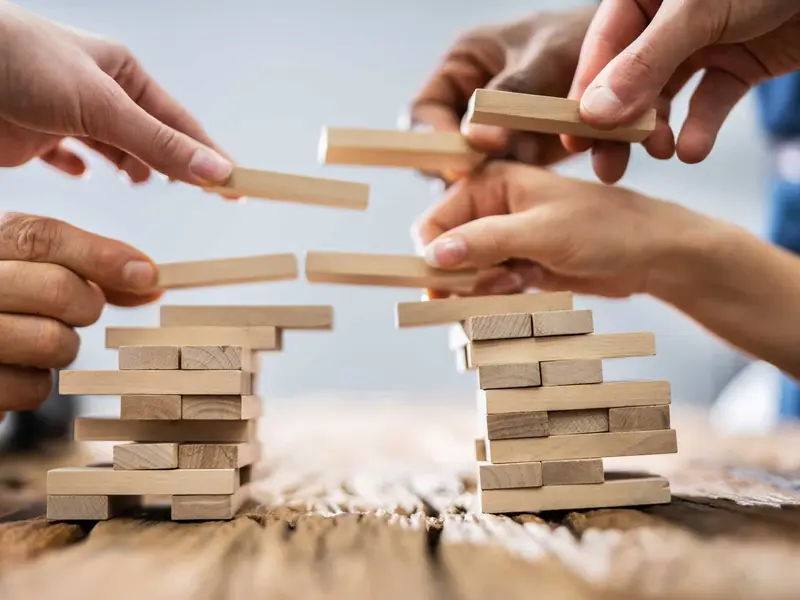 Manos de un equipo construyendo una estructura con piezas de madera